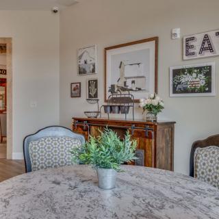 A cozy dining room featuring a round table with upholstered chairs, decorated with plants and framed artwork.
