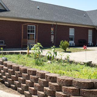 A well-maintained garden area with a brick retaining wall and a residential home in the background.