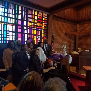 A community gathering inside a church, illuminated by colorful stained glass windows.