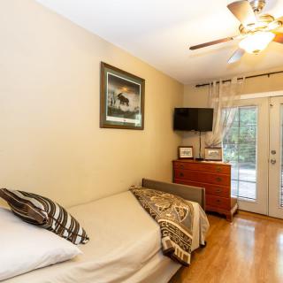 A cozy bedroom featuring a single bed, television, and a glass door leading outside.