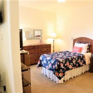 A cozy bedroom with a single bed, floral bedding, dresser, and a standing lamp.