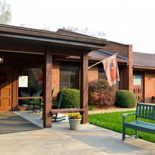 A brick building entrance with a small garden, a flag, and benches.