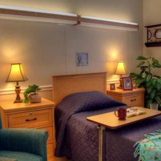 A cozy hospital room with a neatly made bed, bedside tables adorned with lamps and decorations, and an inviting armchair.