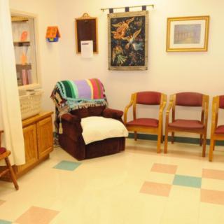 A cozy waiting room with chairs, a colorful blanket on an armchair, and artwork on the walls.