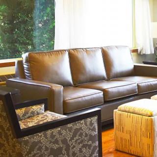 A cozy living room with a leather sofa, patterned armchair, and ottoman near a large window.