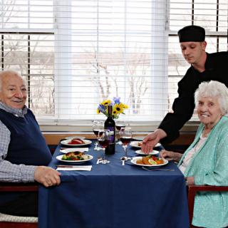 An elderly couple enjoying a meal at a restaurant, served by a waiter.