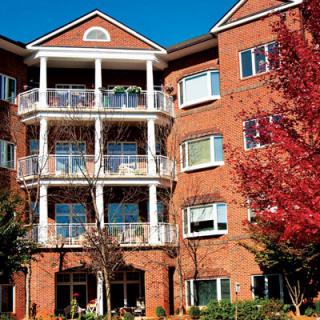 A multi-story brick apartment building with balconies, surrounded by trees with autumn foliage.