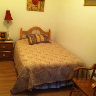A cozy bedroom with a neatly made bed, nightstand with a lamp, and a rocking chair.
