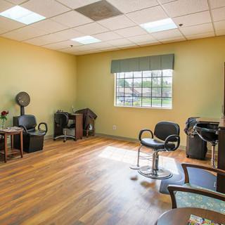 An empty hair salon with chairs and styling equipment, featuring a large window and wooden flooring.