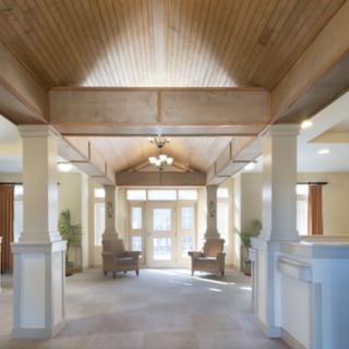 A spacious hallway with wooden ceilings and elegant columns, featuring comfortable seating and ample natural light.