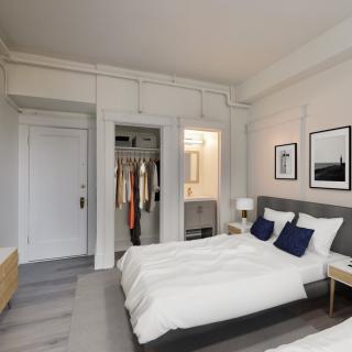 A modern, minimalist bedroom featuring a neatly made bed, wall art, and an open closet.