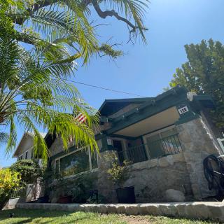 A charming bungalow with a stone facade, surrounded by palm trees on a sunny day.