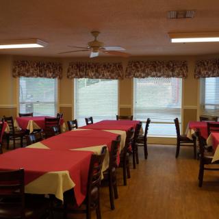 A dining room with tables covered in red tablecloths and chairs arranged around them.