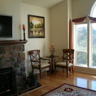 Cozy living room corner with a stone fireplace, elegant chairs, and a large window letting in natural light.