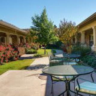 A serene outdoor patio area with tables and chairs surrounded by lush gardens and pathways.
