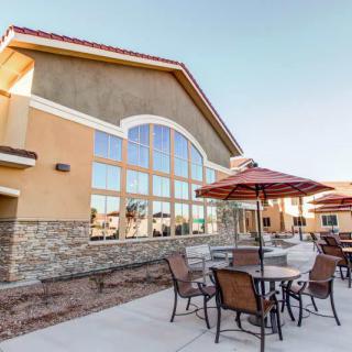 A modern building with a stone facade featuring outdoor seating with tables, chairs, and umbrellas.