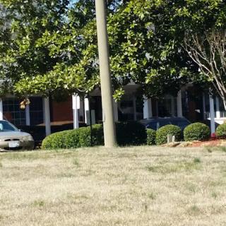A suburban building surrounded by trees and bushes, with parked cars in the driveway.