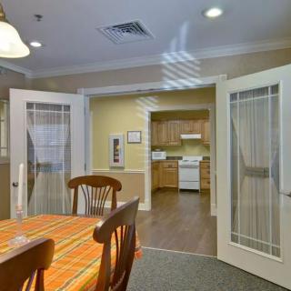 A cozy dining area with a view into the kitchen, featuring wooden furniture and glass doors.
