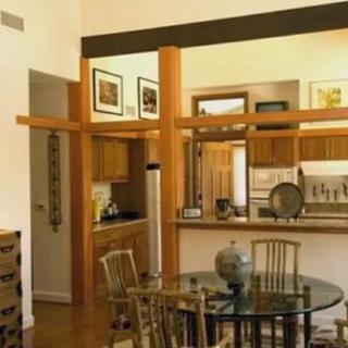 A cozy dining area with a glass table and wooden chairs, adjacent to an open kitchen featuring warm wooden accents and modern decor.