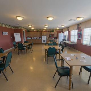 A communal dining area with tables and chairs, featuring a kitchen at the back.
