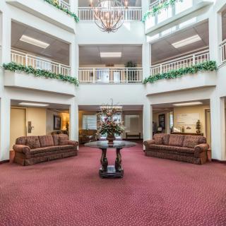 A spacious and elegant atrium lobby featuring sofas, a central table, plants, and a chandelier.