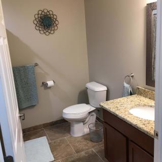 A well-lit bathroom featuring a toilet, sink with granite countertop, and wall decor.