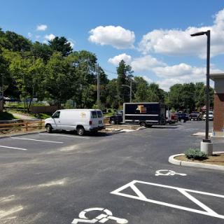 A view of a parking lot with several vehicles and greenery under a blue sky.