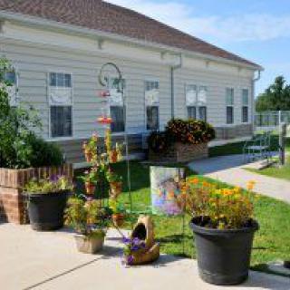 A quaint building with a well-maintained garden featuring various potted plants and flowers on a sunny day.