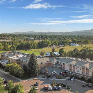 An aerial view of a countryside landscape with buildings surrounded by trees and greenery under a clear blue sky.