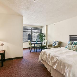 A modern bedroom with a large bed, bedside lamp, table and chairs near a window.