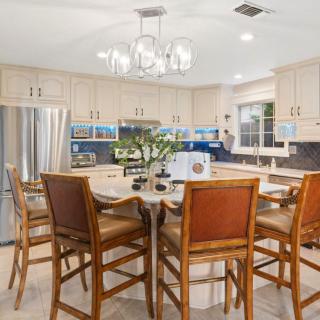 A modern kitchen with a central island, surrounded by wooden chairs and equipped with stainless steel appliances.