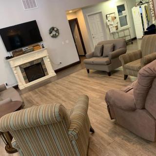 A cozy living room with multiple chairs, a sofa, a television mounted above a fireplace, and a hardwood floor.