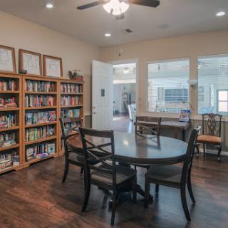 A cozy reading area featuring a table surrounded by chairs and shelves filled with books.