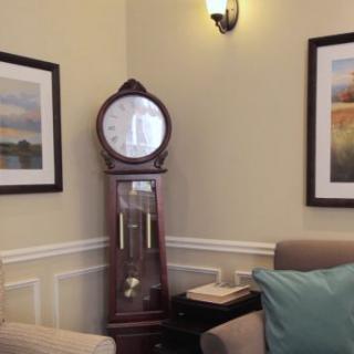 A cozy living room corner featuring a grandfather clock, framed artwork, and a comfortable armchair with a pillow.