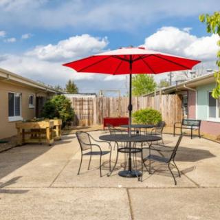 A sunny backyard patio with a red umbrella over a table and chairs.
