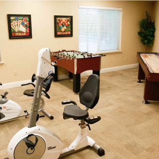 A bright exercise room featuring stationary bikes, a foosball table, and a shuffleboard table.