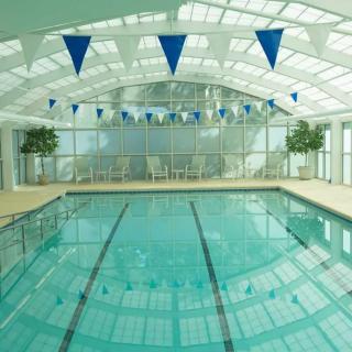 An indoor swimming pool with lanes and blue banners under a glass ceiling, allowing natural light to illuminate the space.