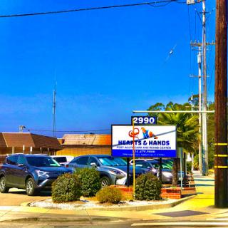 A view of a business featuring a sign and parked cars under a clear blue sky.