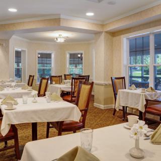 A well-lit dining area with neatly arranged tables and chairs, featuring large windows and elegant decor.