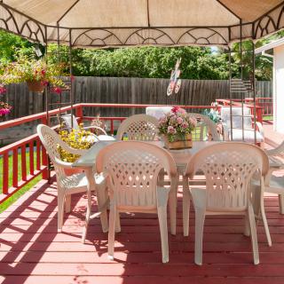 A sunny outdoor patio with a gazebo, featuring a table and chairs surrounded by hanging flowers.