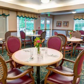 A cozy dining room with elegantly set tables and chairs, adorned with flowers.
