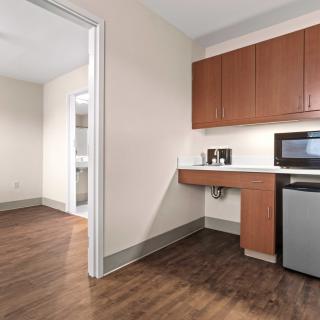 A compact kitchen area in an apartment with wooden cabinets, a small refrigerator, microwave, and wood flooring.