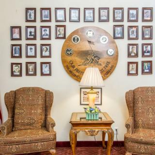 A cozy living room corner featuring two armchairs, a side table with a lamp, and a wall adorned with numerous photo frames and a decorative clock.