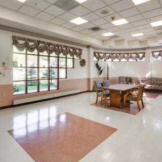 A spacious community room featuring a table and chairs, well-lit with natural light from the windows.