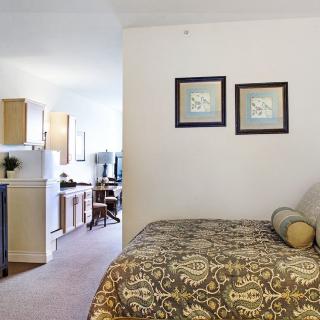 A cozy studio apartment featuring a bed with patterned bedding and a kitchenette in the background.
