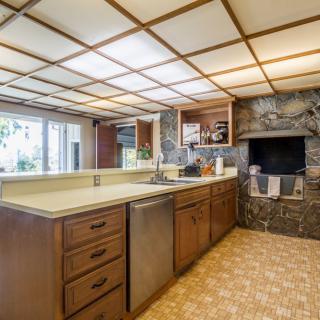 A retro-style kitchen featuring wood cabinets and a stone fireplace, with an island counter and overhead lighting.