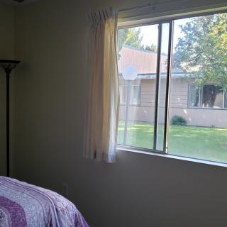 A bedroom with a bed and lamp, featuring a window with a view of the outdoors.