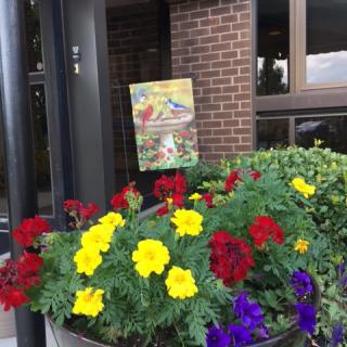 A vibrant display of red, yellow, and purple flowers in a planter outside a brick building.