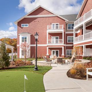 A sunny day at a residential building with brick exterior and well-maintained landscaping, featuring balconies and a walking path.