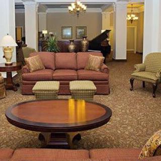 A hotel lobby featuring a comfortable seating area with sofas and armchairs, elegant chandeliers, and a grand piano in the background.